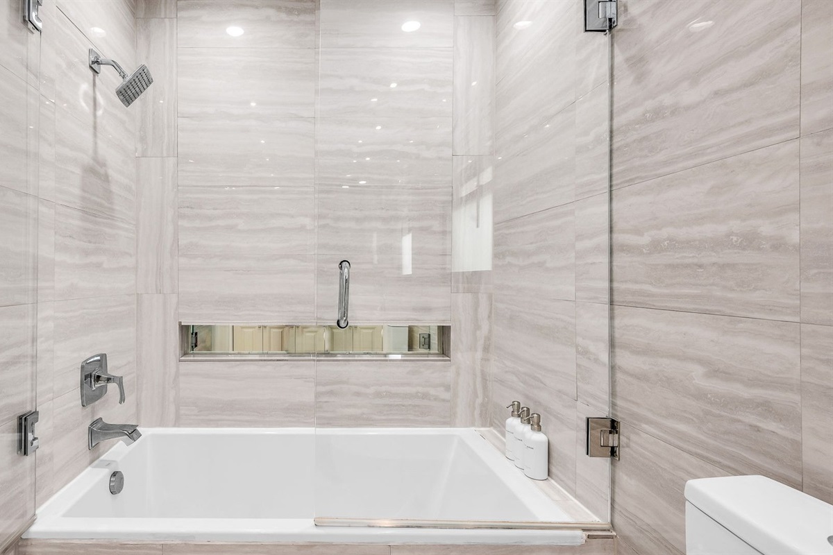 The ensuite bathroom features a sleek double vanity, elegant stone finishes, and a spa-like shower/tub combo with glass enclosure. Designed for both style and comfort, it’s the perfect space to refresh and unwind