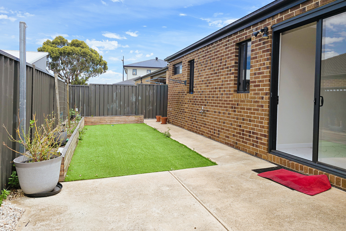 Sliding doors open to a secure backyard with artificial turf, garden edging and a paved patio area connected to the home.