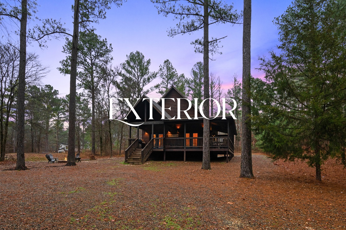 A wider exterior shot captures the peaceful forest setting that surrounds the cabin on all sides.