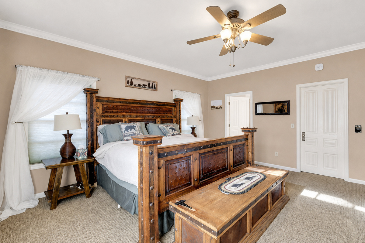 Primary bedroom with rustic wood bed, ceiling fan, bedside lighting, and warm cabin-style details for a restful stay.