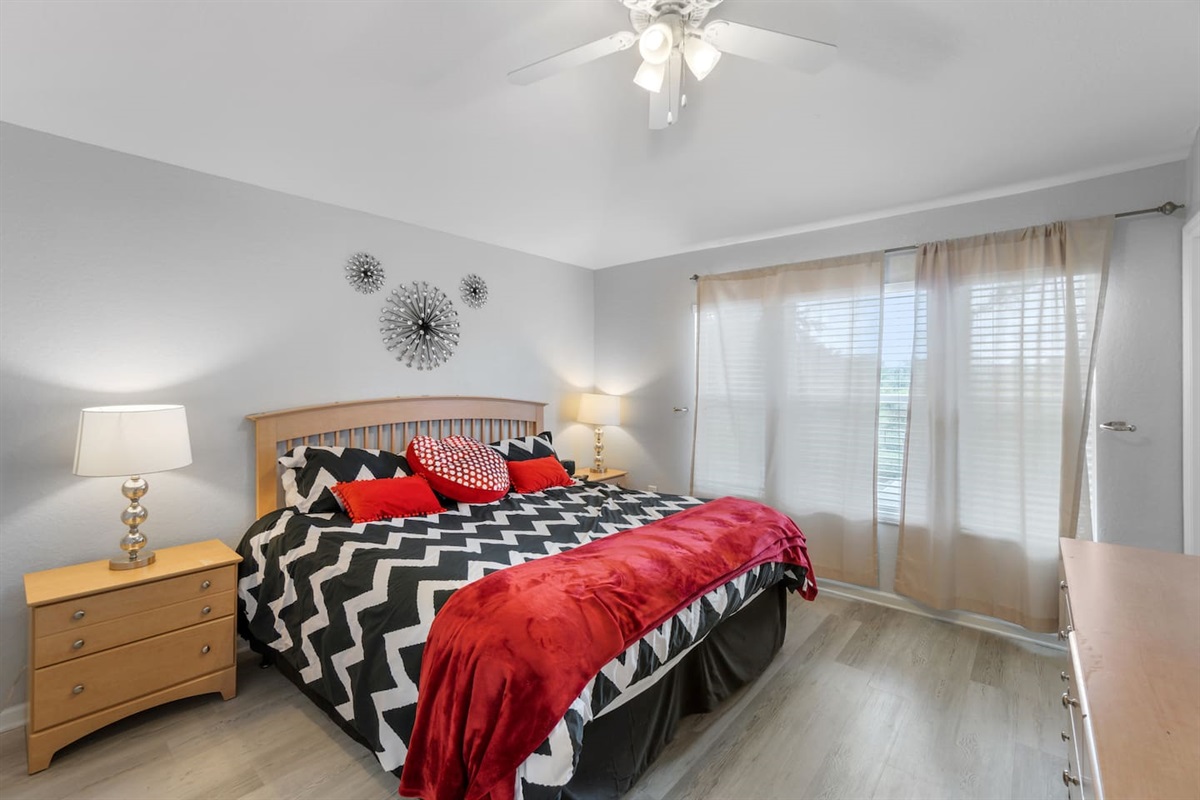 - Spacious bedroom with king bed, bold chevron bedding, and red accent throws  
- Large windows with sheer curtains let in soft natural light for a calm feel  
- Stylish wall art and nightstands with lamps enhance the cozy retreat  
