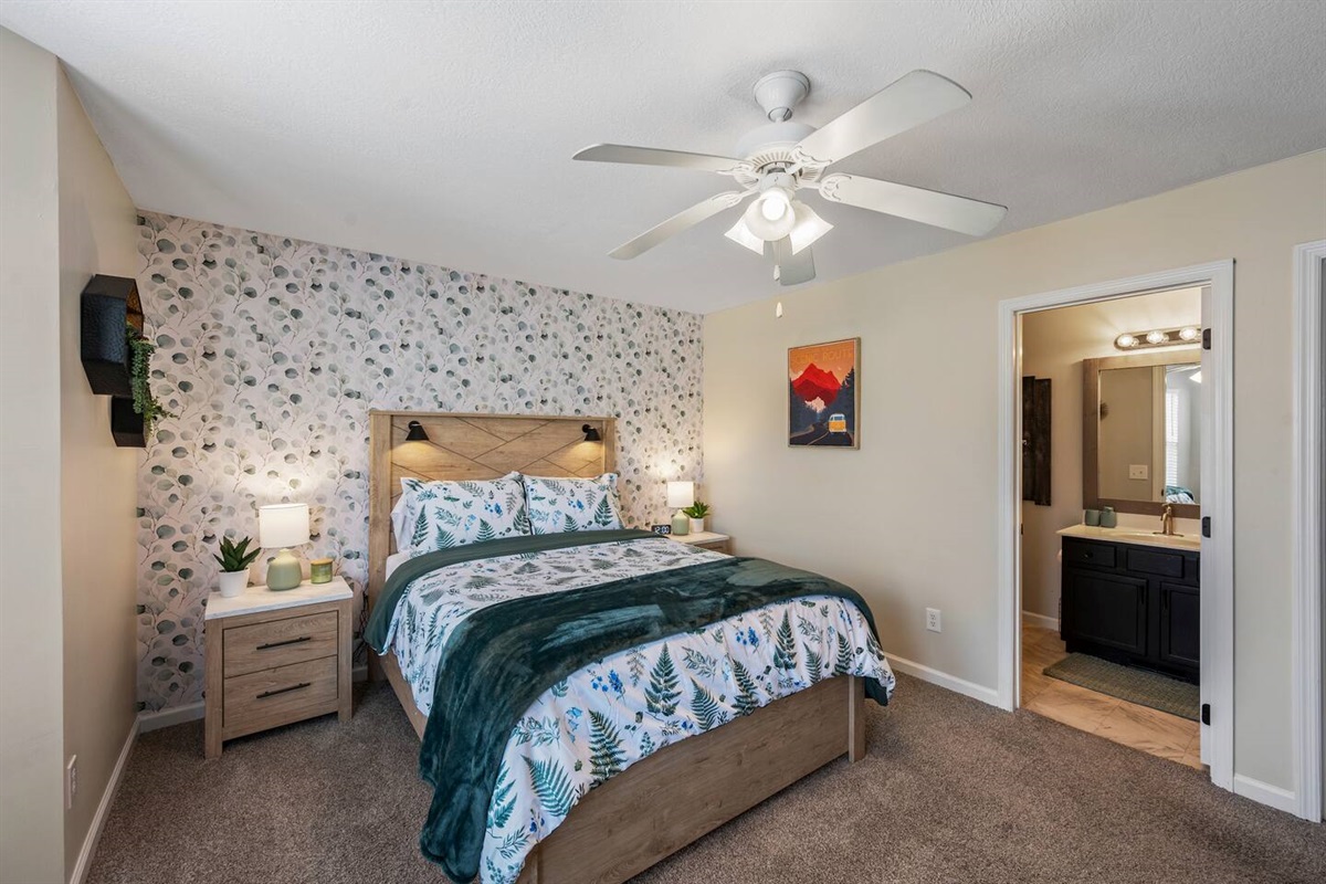Inviting bedroom with a queen bed, accent wallpaper, cozy lighting, ceiling fan, and private en-suite bathroom—perfect for a comfortable stay.