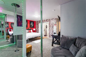Experience comfort and flair in this serene master bedroom, featuring a luxurious king-sized bed, bold red walls, unique artwork, and a fun stripper pole for a playful touch!