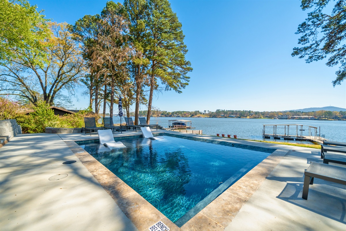 Bask in the sunshine as the pool reflects the surrounding trees and blue sky, creating a bright and refreshing outdoor escape.