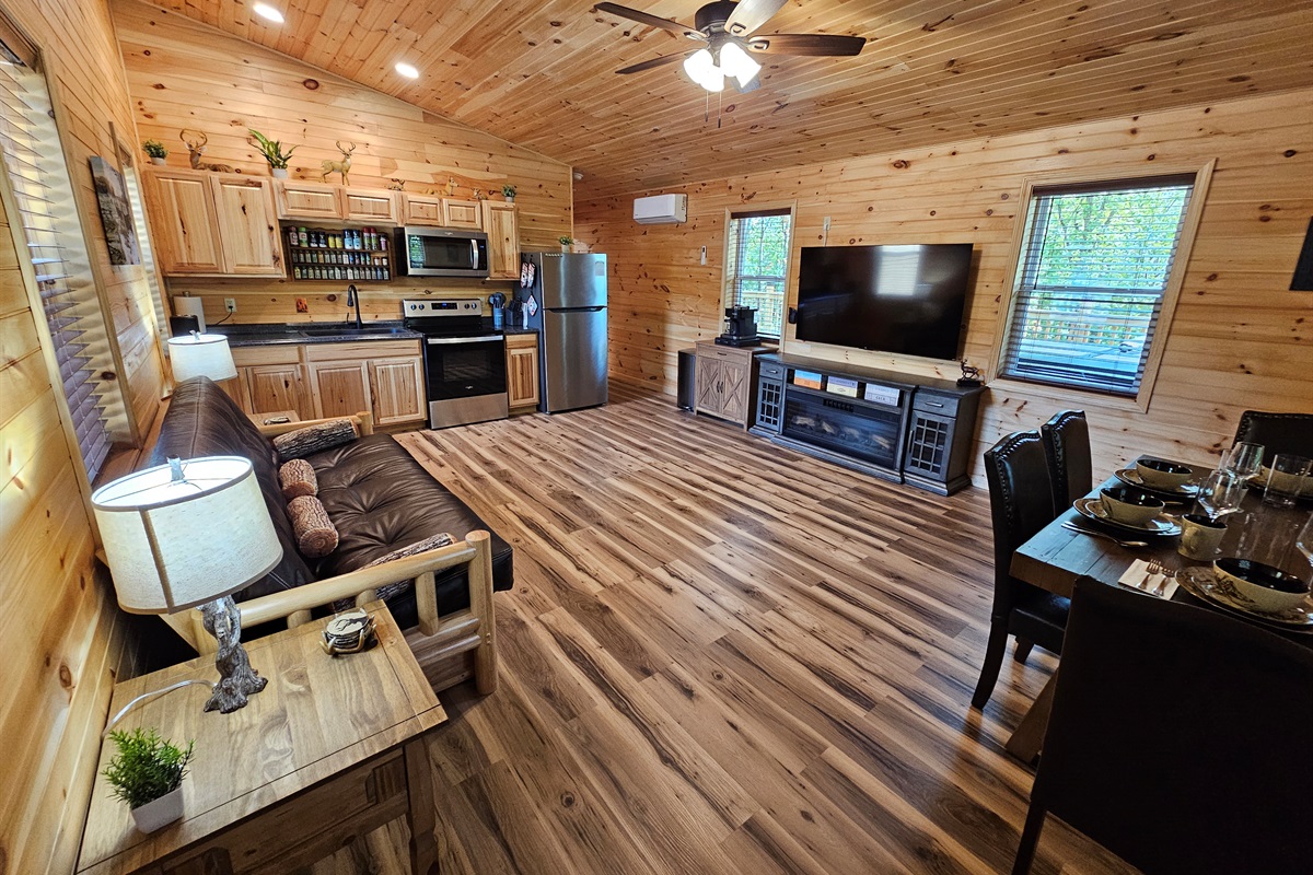 Open living area with futon, dining table, large TV, and full kitchen with stainless steel appliances.