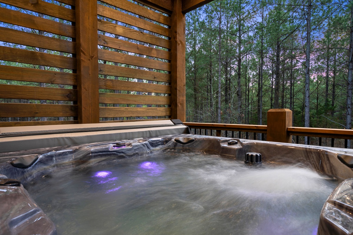 The bubbling hot tub sits on a quiet deck surrounded by trees, creating the perfect place to soak, unwind, and enjoy the peaceful sounds of the forest.