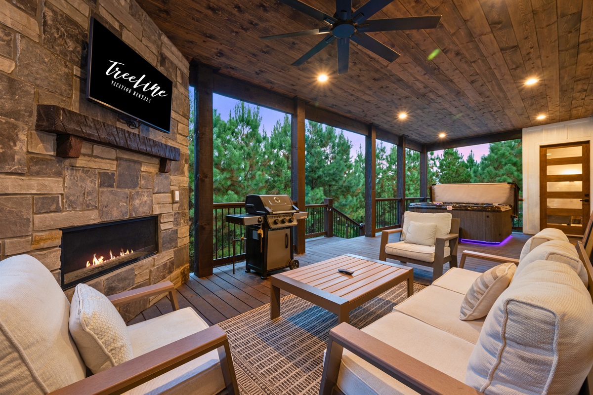 Covered outdoor living room with fireplace, TV, and cozy seating.