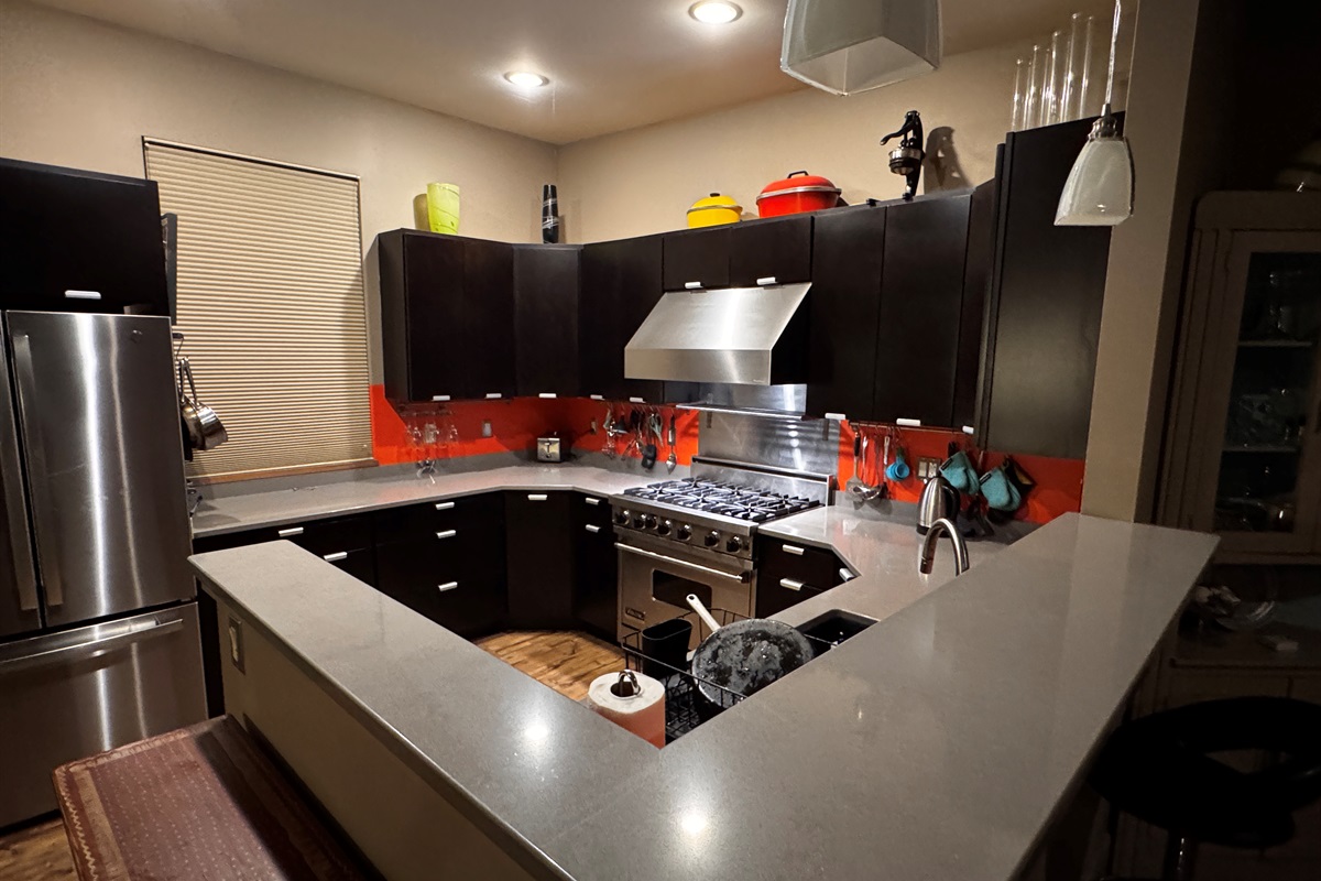 Open-concept main floor looking over the breakfast bar toward the chef’s kitchen and dining area. This central hub connects the living spaces to the staircase, providing a seamless flow for groups staying at our Mount Desert Island retreat.