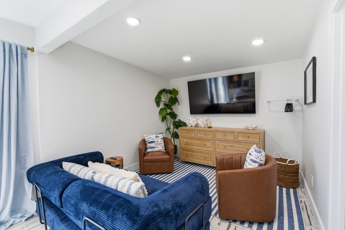 A plush navy sofa, cognac leather chairs, striped nautical rug, and a large flat screen make this the perfect spot to unwind in the master bedroom.