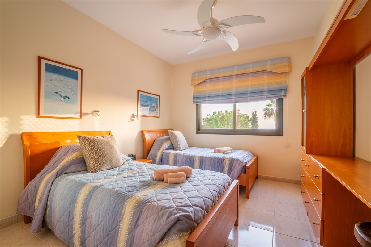 Twin bedroom with a window facing the back garden and swimming pool. The room has spacious closets, a ceiling fan, a dedicated AC/heating unit, and a Bluetooth-enabled speaker/alarm clock combo.