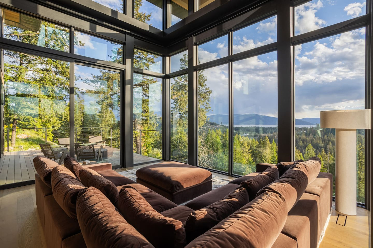 The living room on the main floor enjoys a comfortable couch immersed in floor to ceiling windows with views from mountain to lake and then over to Schweitzer. 