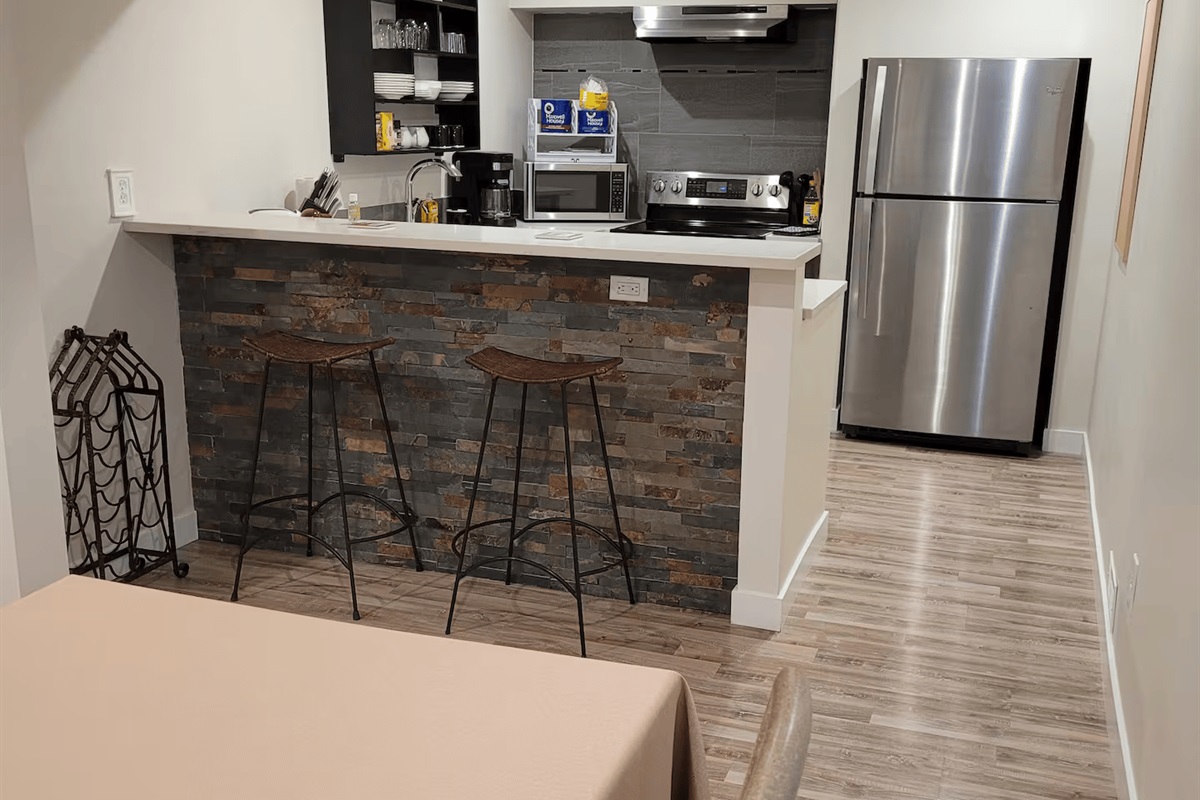 Looking from the dining area into the kitchen. Full size refrigerator, dishwasher, oven, coffeemaker, toaster and microwave. Counters and breakfast bar in white & grey quartz