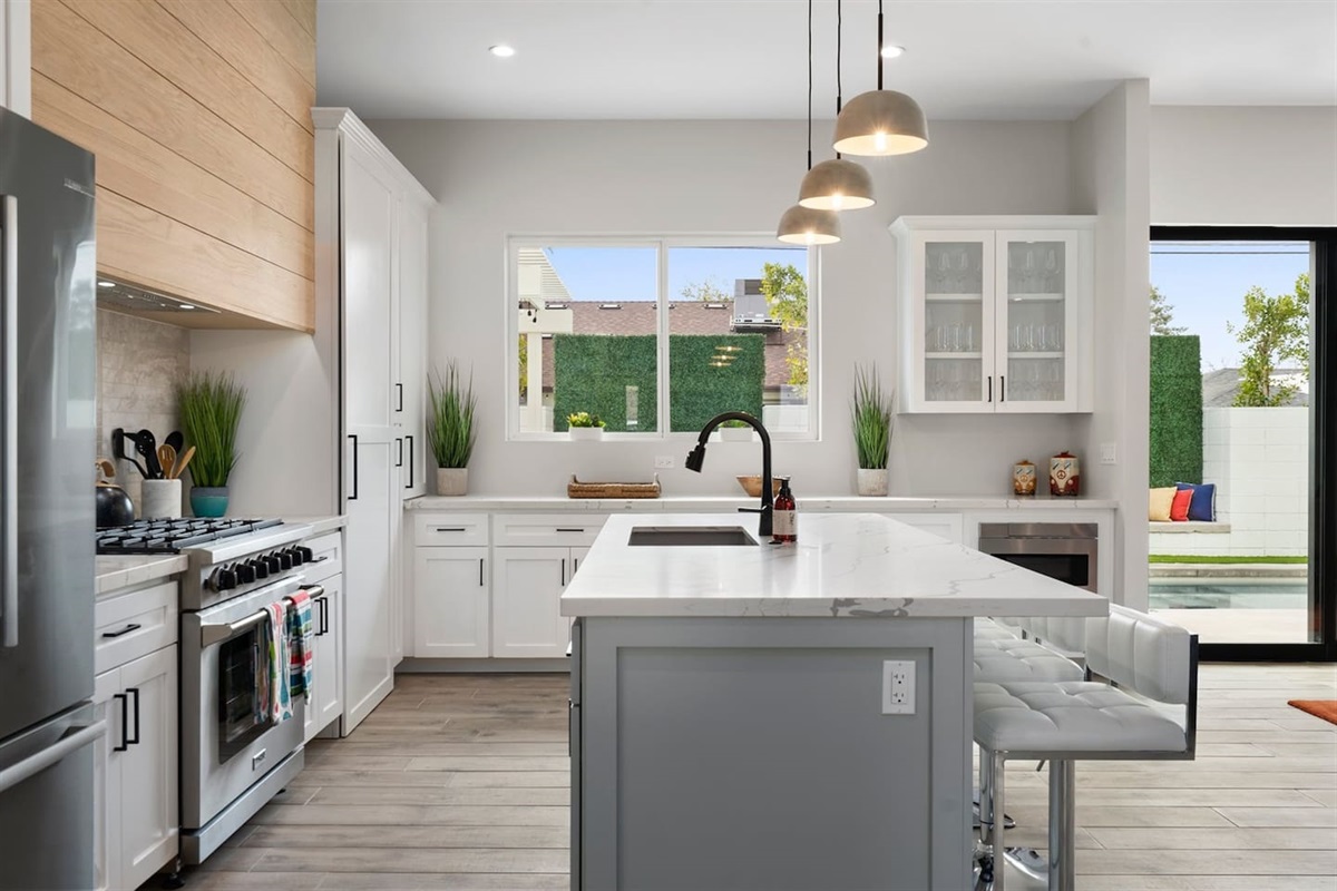 Cook in style with this full kitchen, featuring a spacious island, gas range, wine cooler, and coffee area. White decor with marble, green, and wood accents adds elegance to your culinary experience.