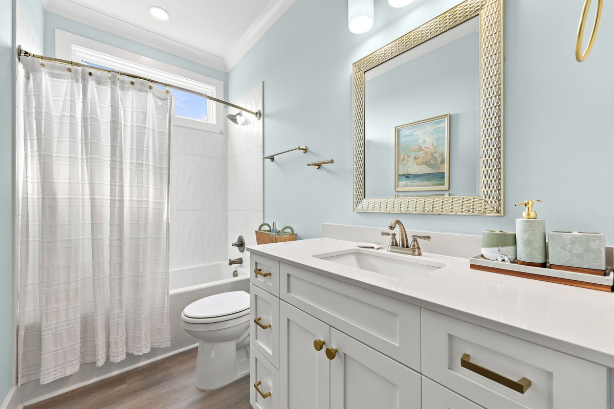 A clean and modern guest bathroom with a spacious vanity, bathtub/shower combination, and elegant coastal finishes for added comfort during your stay