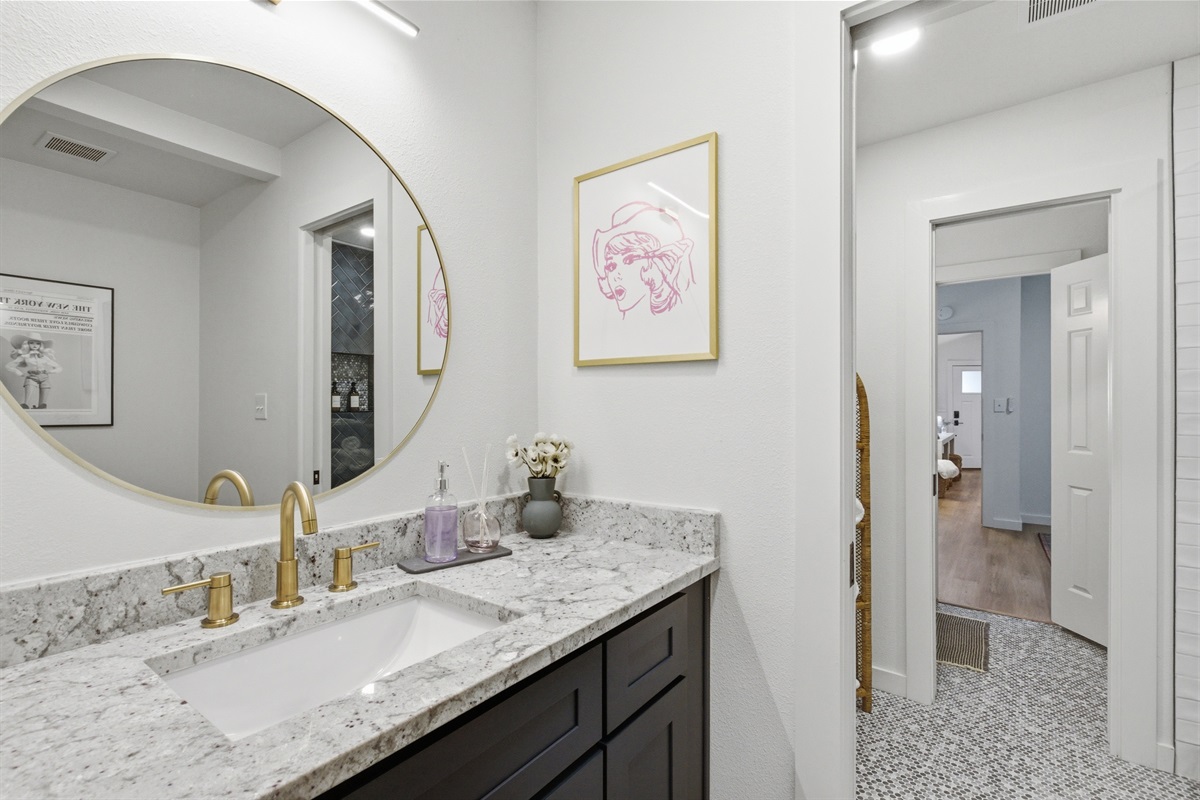 Marble vanity with gold hardware and round mirror. Hairdryer provided. Stocked with all bath essentials by Ginger Lily Farms. Shared bathroom serving Bedrooms 3 and 4, Arlington TX.
