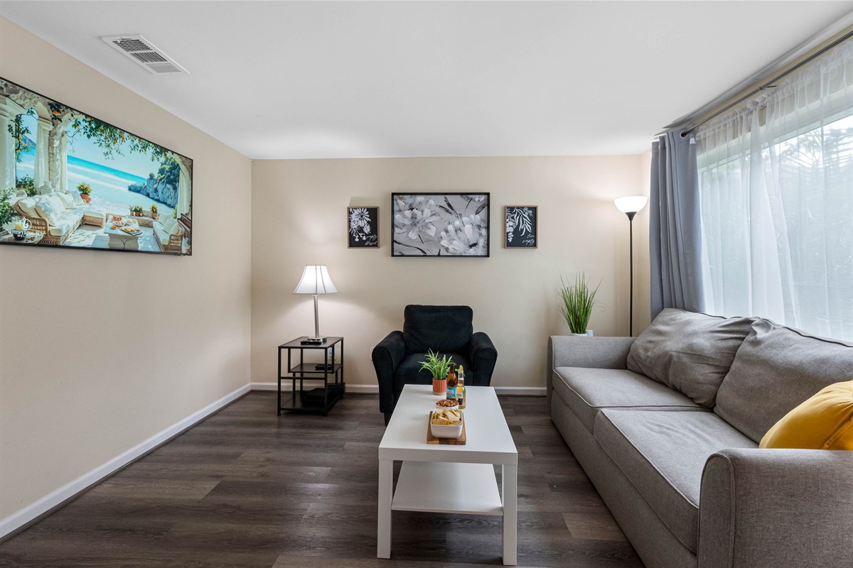 Hardwood-style floors bring warmth and texture to the room, while a sleek table lamp by the door enhances the cozy ambiance for evening lounging or reading.