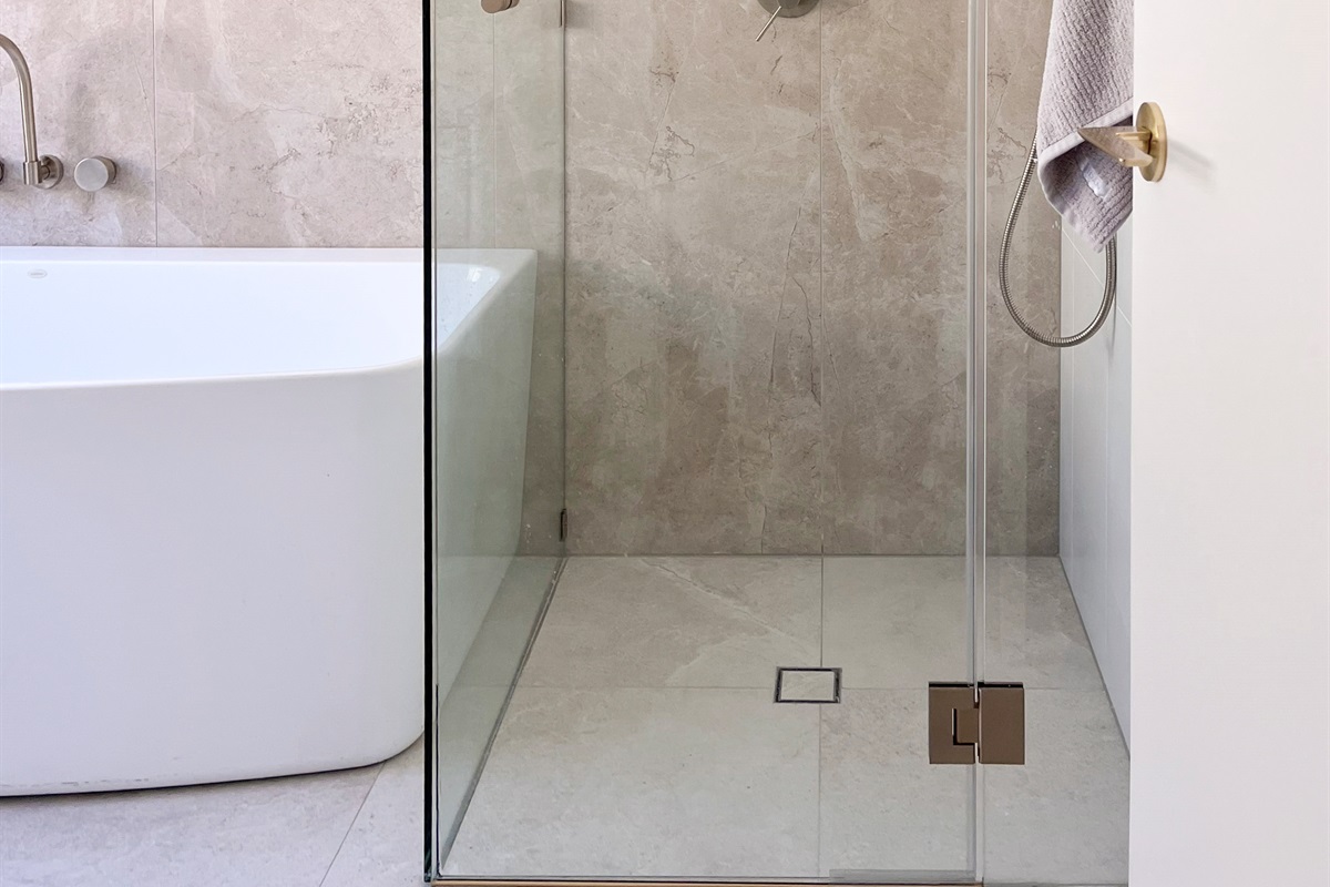 This bathroom combines a deep bathtub, walk-in shower, toilet and vanity in one practical space with neutral tiling.