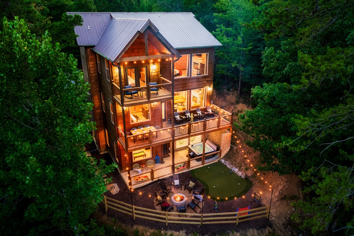 Luxury cabin with multiple decks with string lights, hot tub, and backyard with fire pit and mini golf