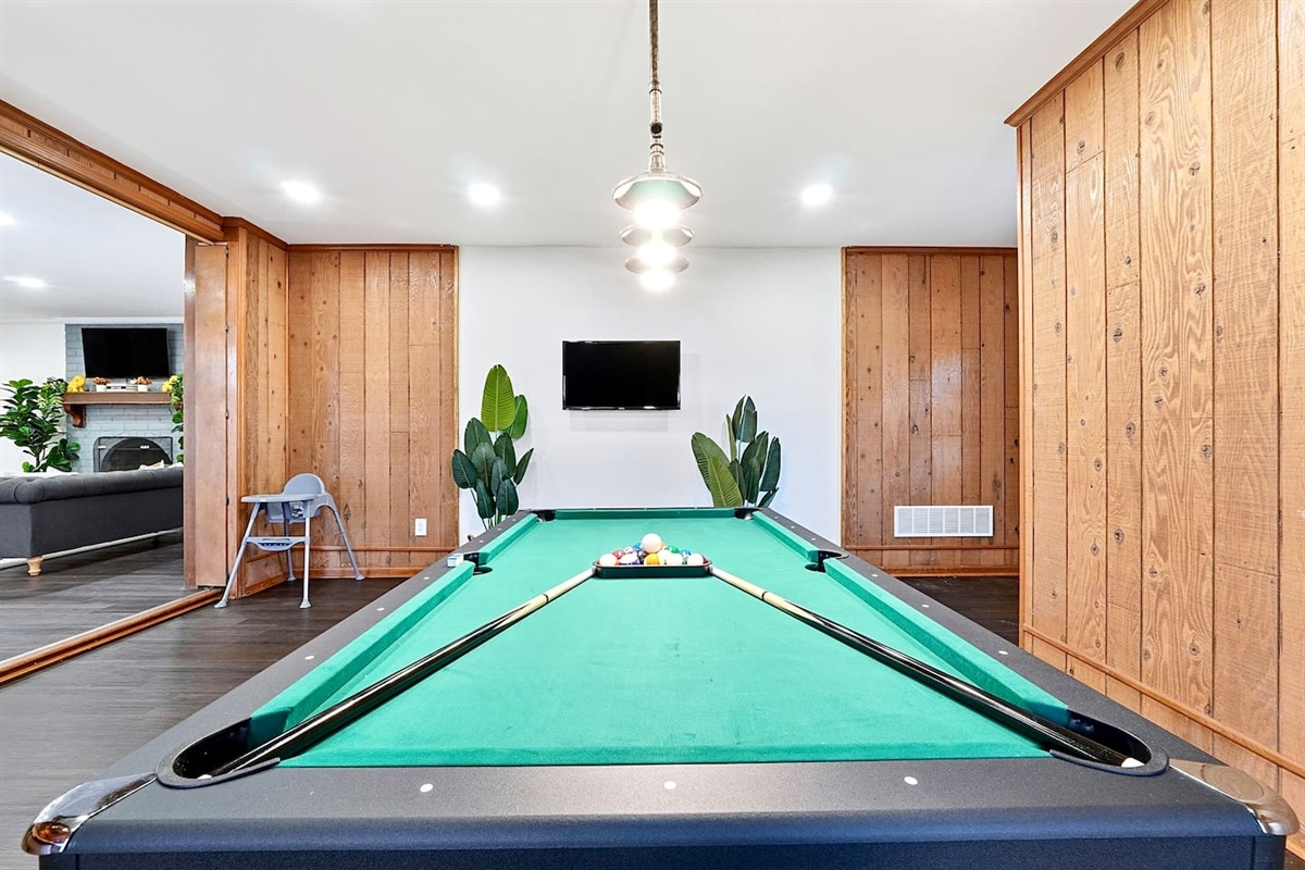 Enjoy this main-floor game room near the side entrance featuring a convertible pool and ping-pong table, a custom curved wood bar, and a Roku powered smart TV—ideal for entertaining and casual gatherings.