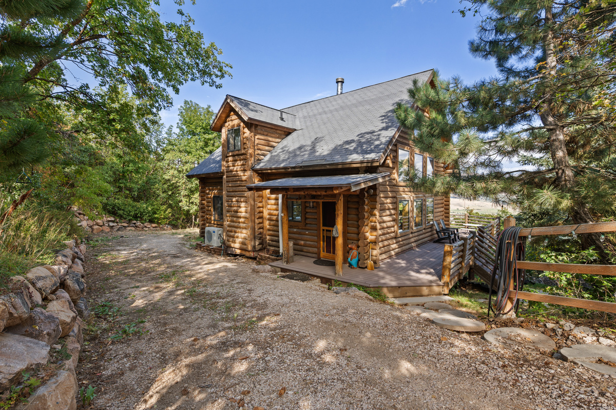 Welcoming front approach to the rustic log cabin surrounded by mature trees.