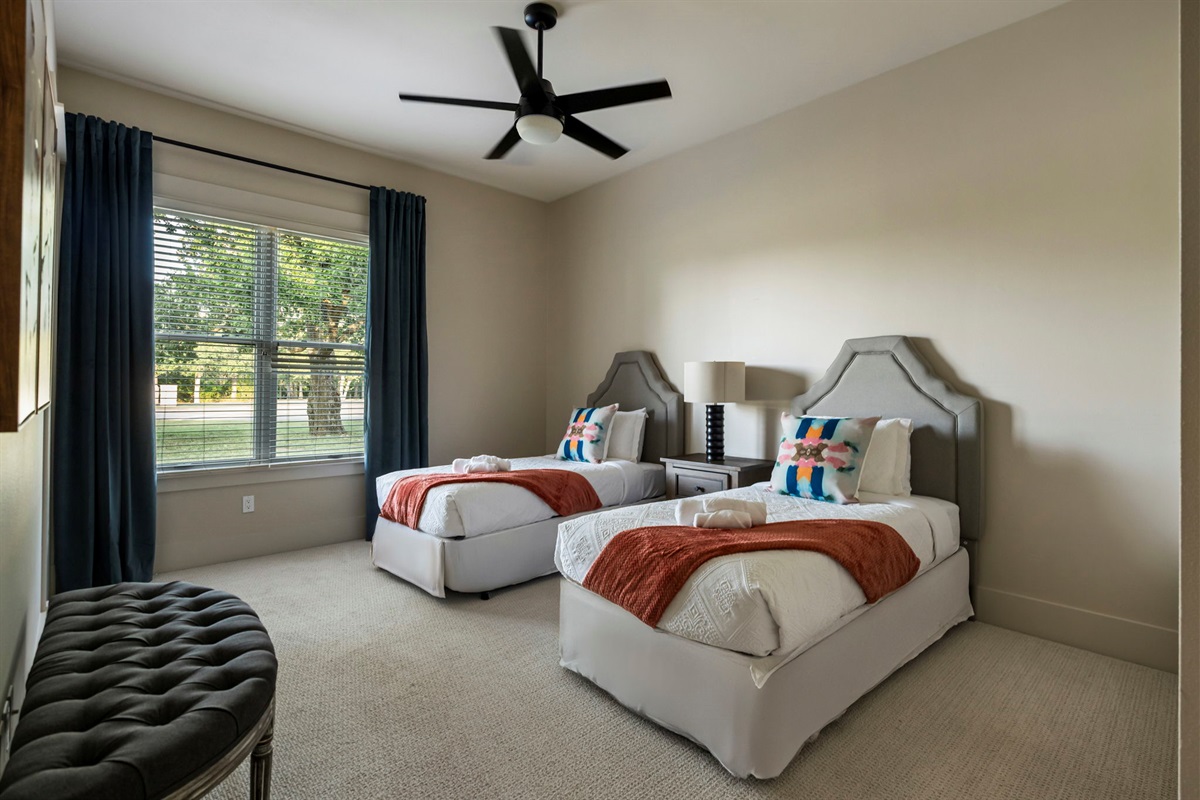 Bright and comfortable with two twin beds, a ceiling fan, and a lamp, making it a cozy space for family or friends.
