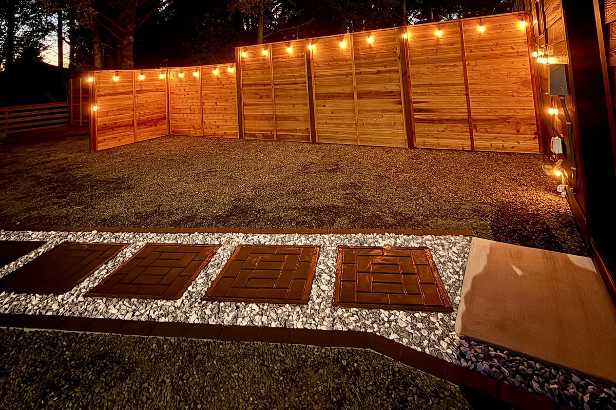 Follow the glowing paver path along the string-lit fence — after dark this stretch of the yard feels like its own private hideaway.
