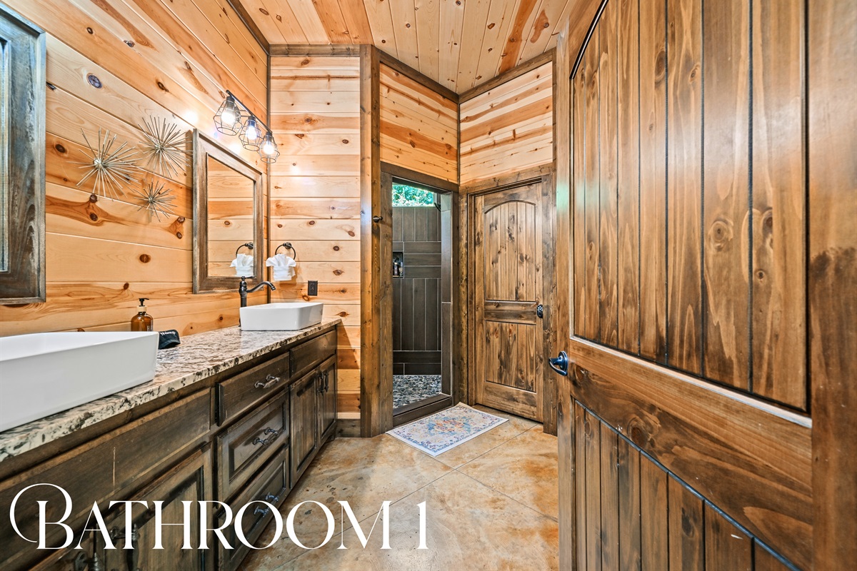 Bathroom 1 is beautifully appointed with double vanities, warm wood finishes, and modern lighting.