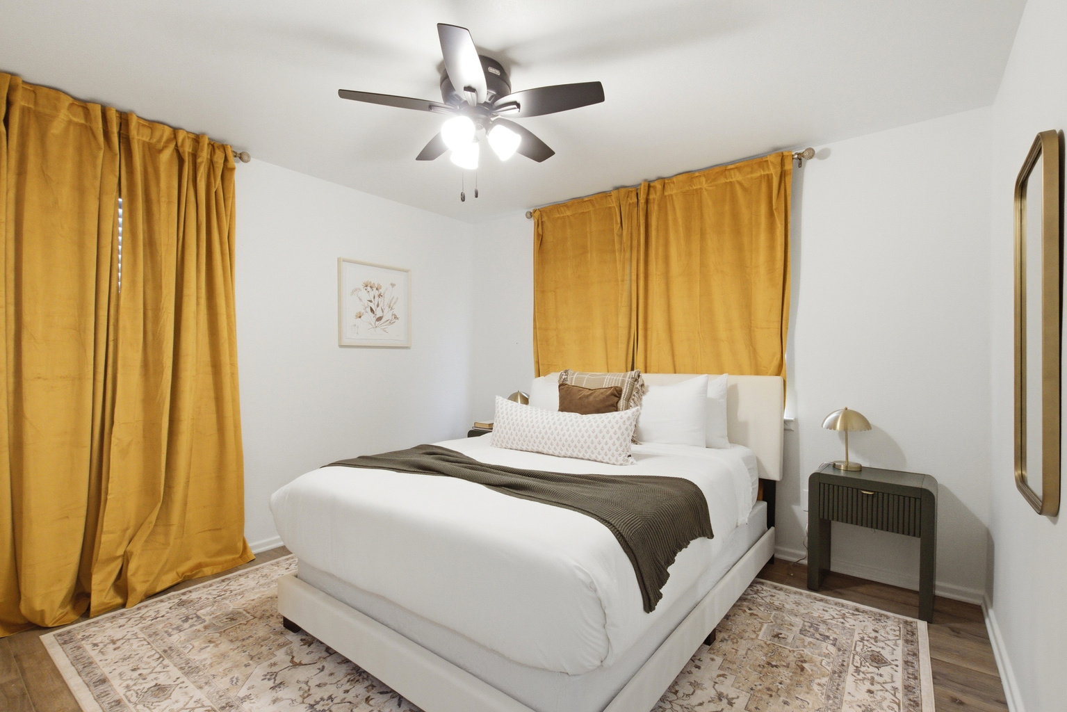 Bedroom 3 with Queen Bed, golden curtains, and Ceiling Fan. Bright and airy with Smart TV, fresh Bed Linens, and Clothing Storage. Sleeps two comfortably.
