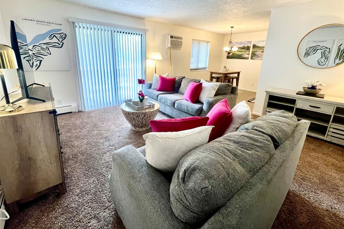 Bright and inviting living area with comfy seating, colorful accent pillows, and natural light pouring in through large sliding doors. Enjoy a cozy night in with the smart TV or gather with friends around the stylish coffee table and open dining space