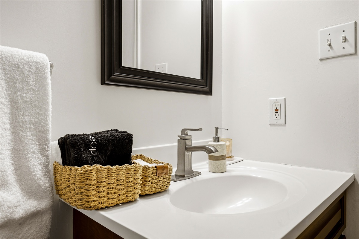 Bathroom vanity stocked with fresh white towels, hand soap, and a woven amenity basket. Clean, minimal, and ready for guests from day one.