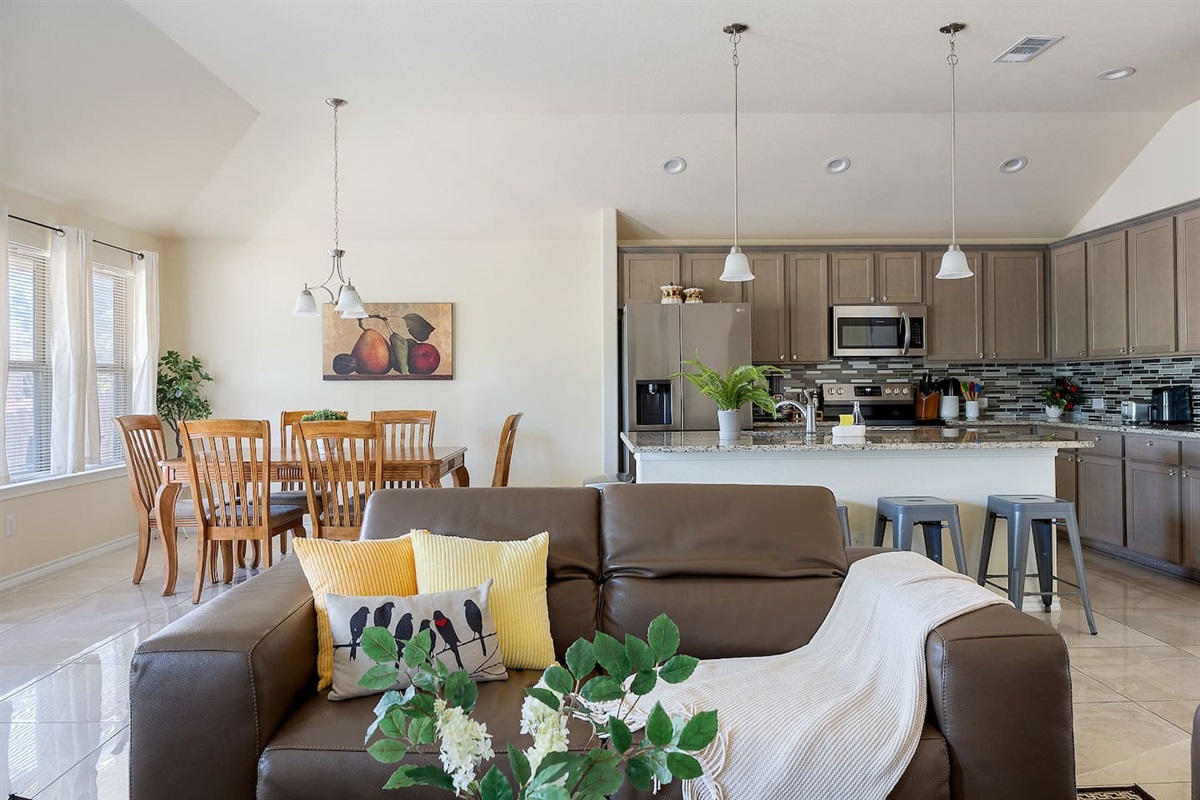 Step into a bright living space with a stylish leather sofa, seamlessly flowing into a dining area and contemporary kitchen.