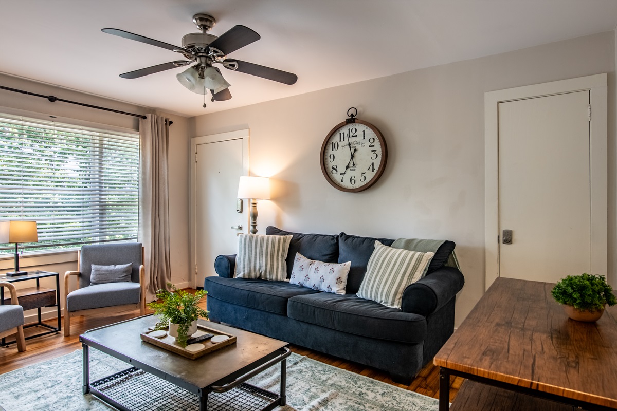 Charming living area with ceiling fan, stylish sofa, and unique clock accent—ideal for lounging or entertaining.