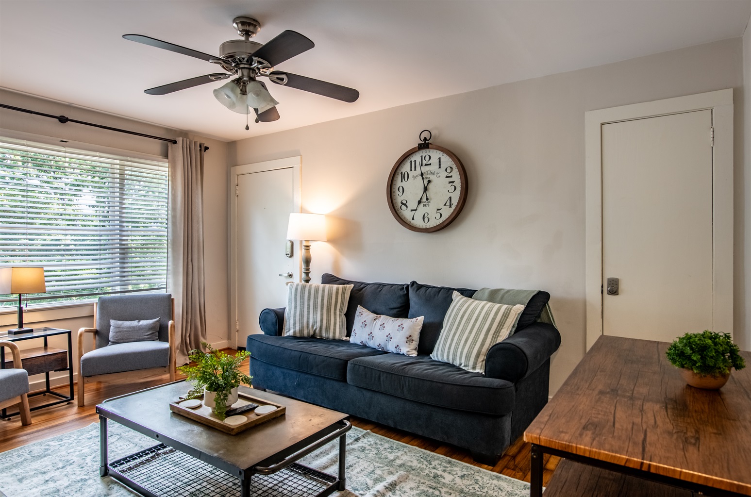 Charming living area with ceiling fan, stylish sofa, and unique clock accent—ideal for lounging or entertaining.