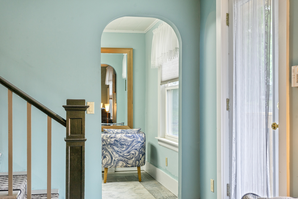 Step through the charming arched doorway into the quiet compass den. Located just off the main living area and staircase, this cozy separate space offers a peaceful retreat featuring a stylish accent chair and a full-length mirror to unwind.