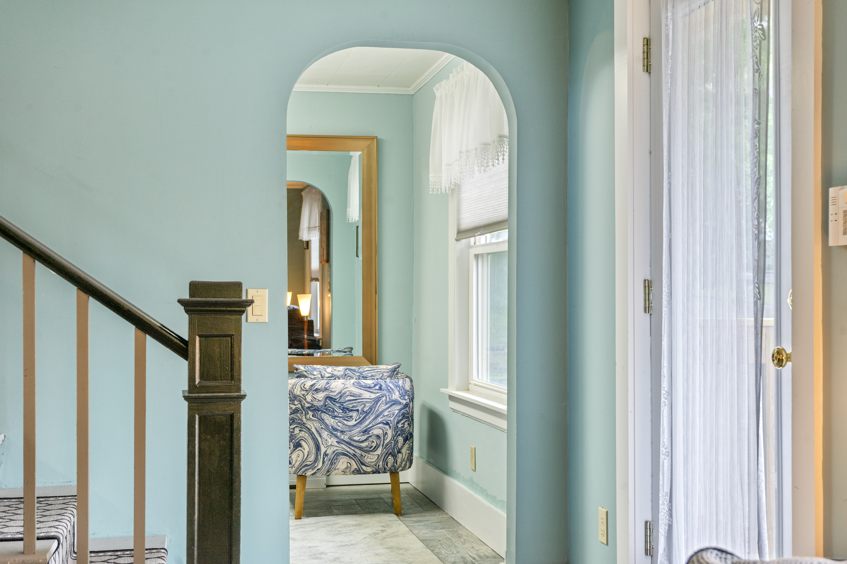 Step through the charming arched doorway into the quiet compass den. Located just off the main living area and staircase, this cozy separate space offers a peaceful retreat featuring a stylish accent chair and a full-length mirror to unwind.