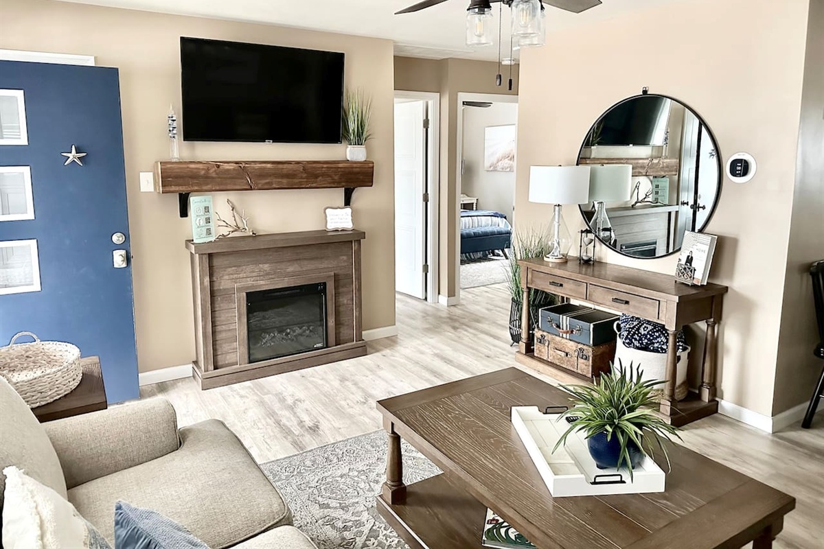 Relax in our beautifully designed living area, featuring a cozy electric fireplace and a large flat-screen TV. The room offers a warm, inviting atmosphere with rustic wood accents, comfortable seating, and a stylish console area—perfect for winding down af