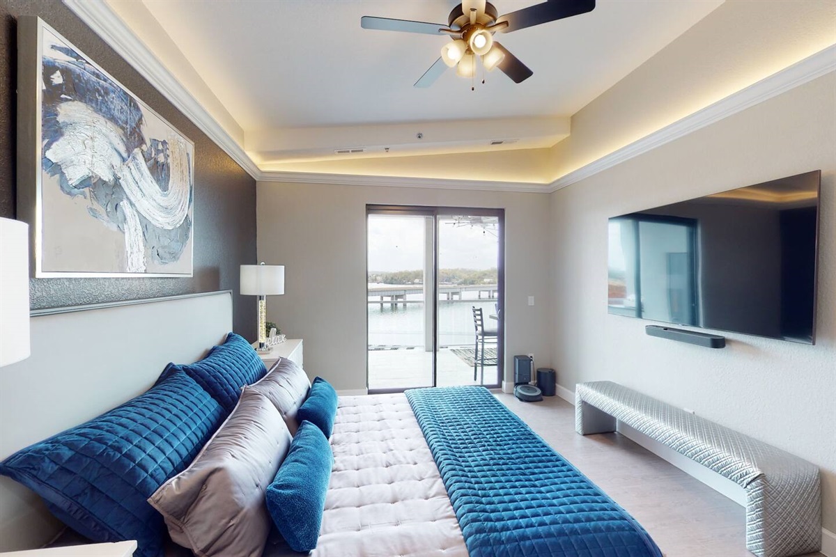 Master bedroom with modern decor, King size bed, private ensuite bathroom, large flat screen tv, surround sound system, ceiling fan, soffit lighting, sliding glass door, and access to the outdoor patio deck.