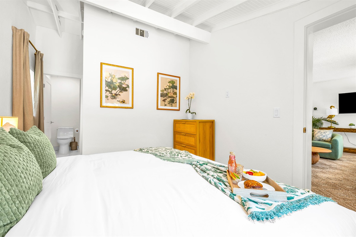 Serene ensuite primary king suite featuring a plush bed with luxury linens, vaulted ceilings with exposed beams, and elegant coastal décor. Includes a spacious walk-in closet with washer and dryer for added convenience and comfort.