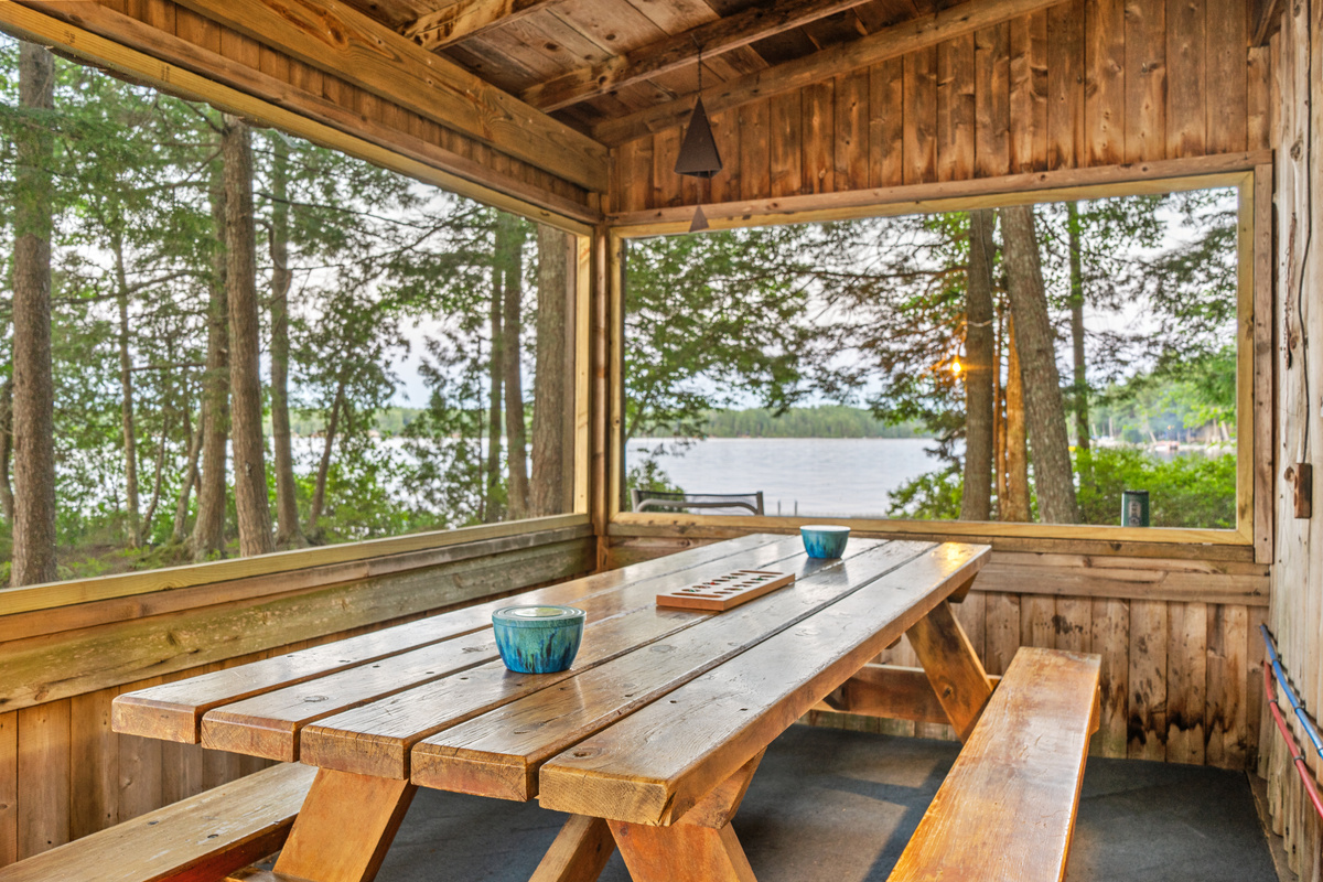 This is a gorgeous close-up corner shot of the picnic table! It really highlights the panoramic nature views—framed by wall-to-wall screen panels looking out over the water and pines on Beech Hill Pond—making it look like the ultimate spot for morning coff
