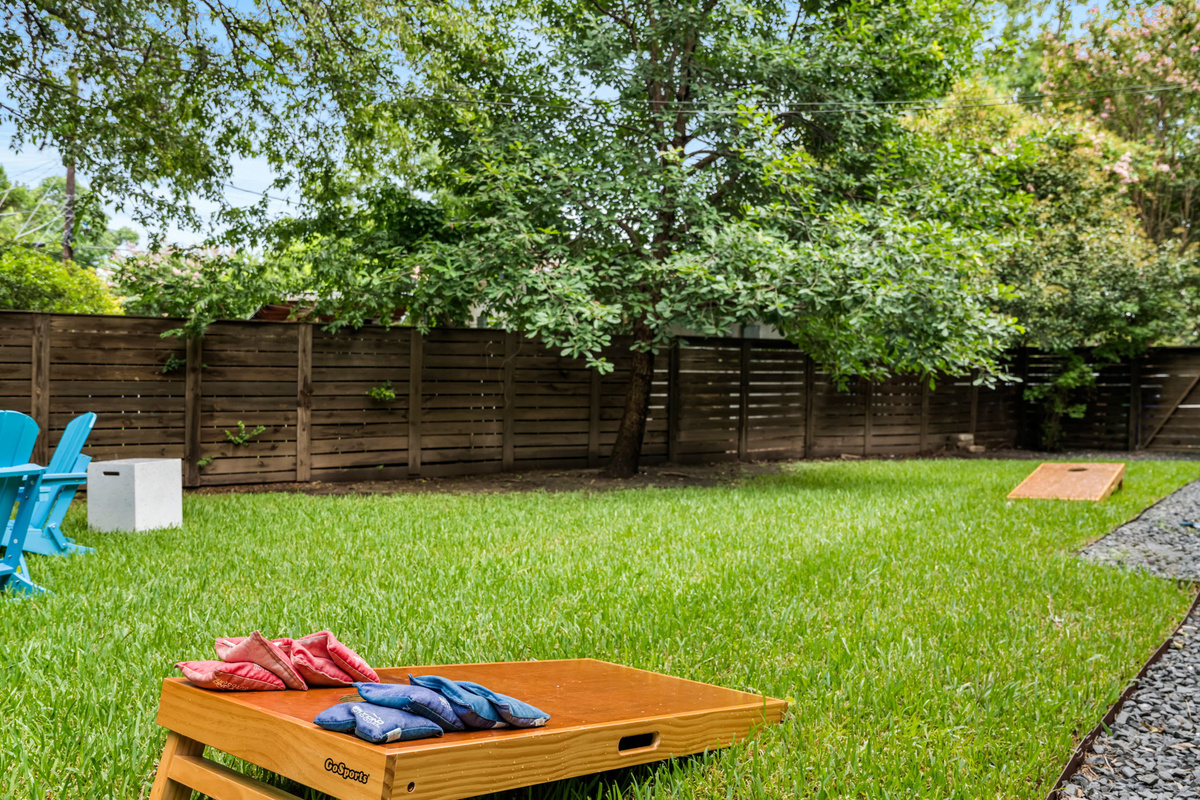 Expansive private backyard with lush lawn and cornhole set ready for outdoor fun — great for families and group gatherings