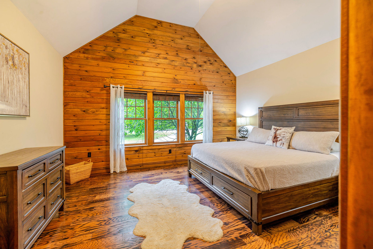 Main-floor primary suite features a king bed, high ceiling, and peaceful woodland views.