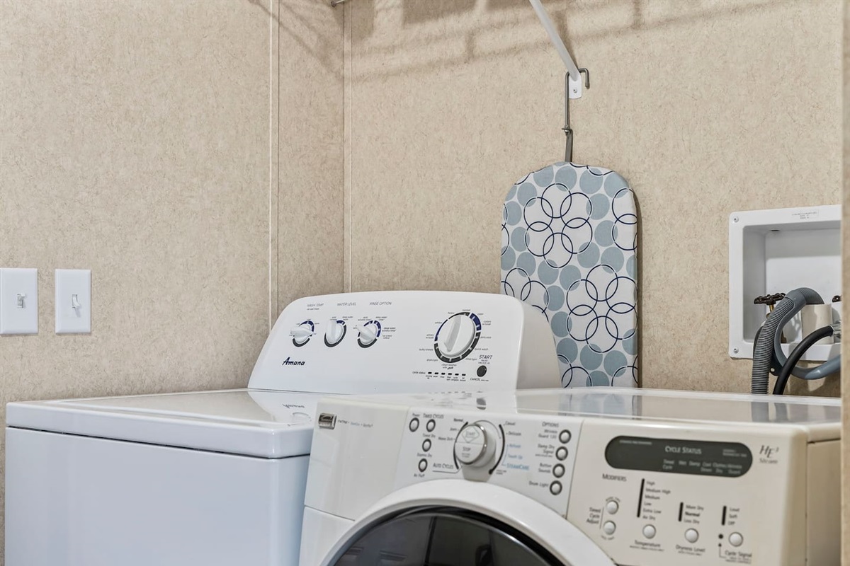 Fully equipped laundry area featuring modern appliances, storage shelf, and ironing essentials for guest convenience.
