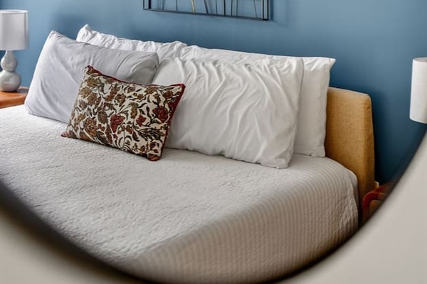 Peaceful bedroom with plush bed, crisp linens, and designer accents. Blue feature wall and modern décor create a calm retreat, ideal for restful nights during your Des Moines stay.