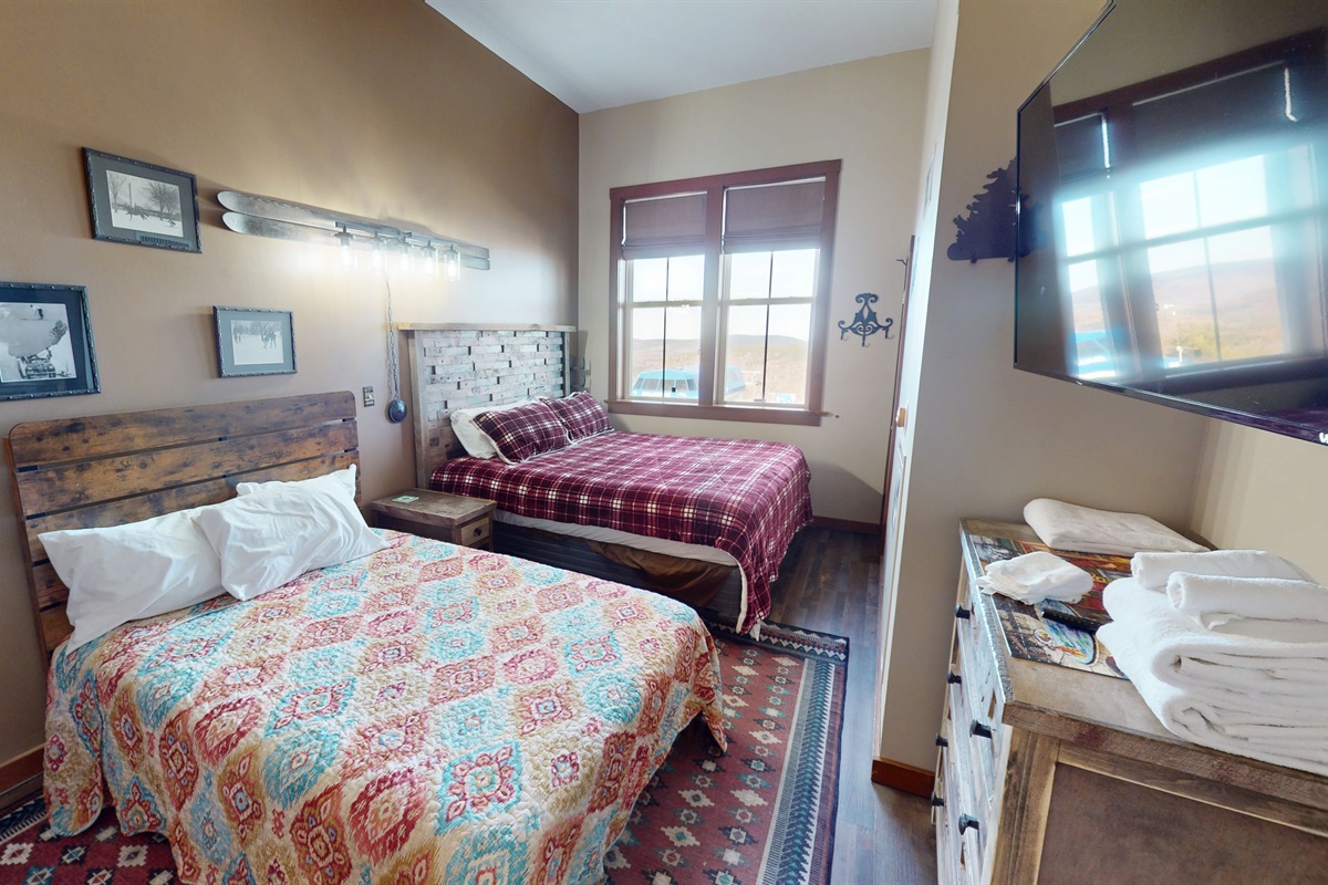 Warm, rustic bedroom with King and full beds and mountain views — comfort meets adventure.