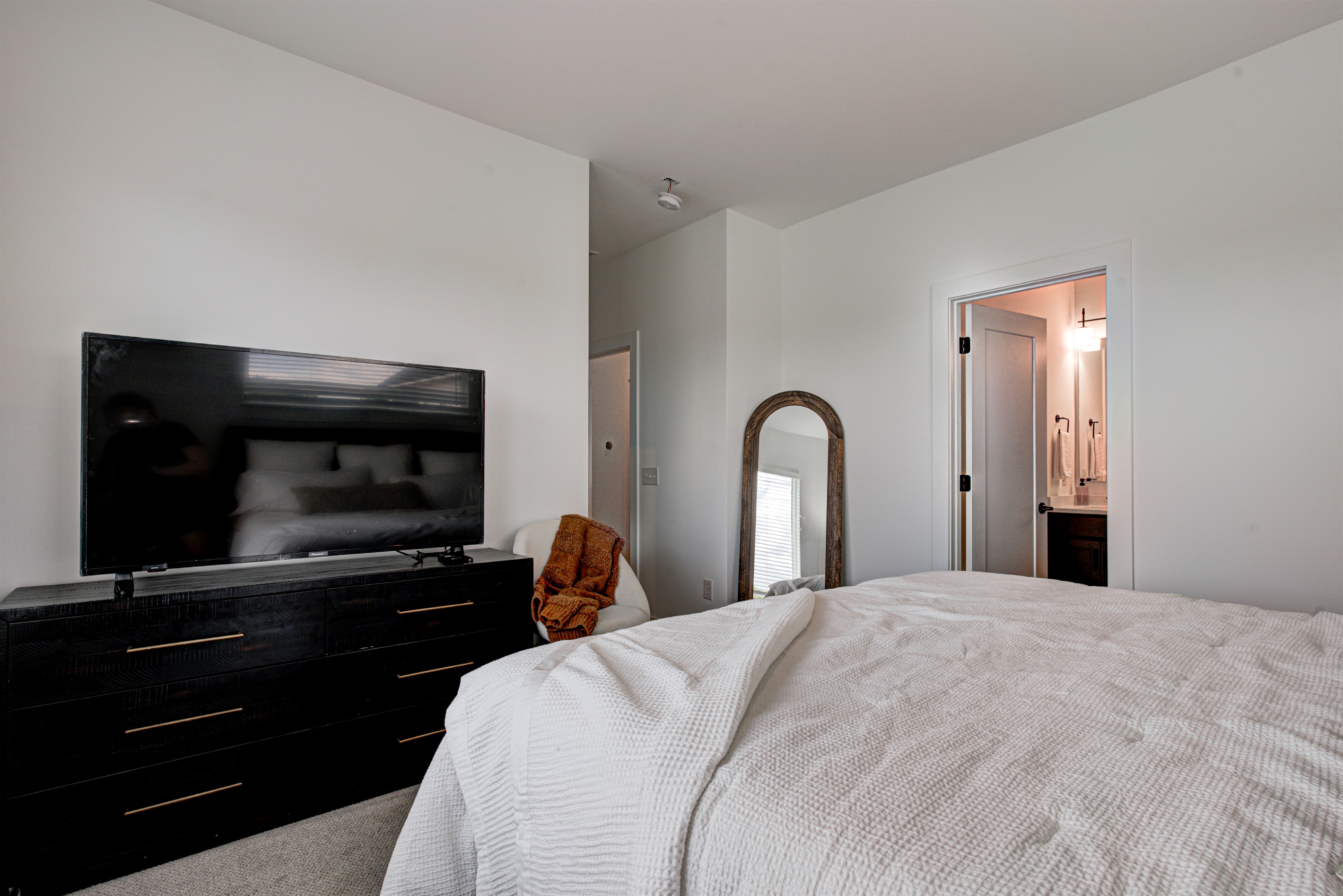 Relax in the serene master bedroom featuring a comfortable king-size bed, soft linens, and cozy pillows. Includes nightstands, lamps, walk-in closet, and full-length mirror for added comfort.