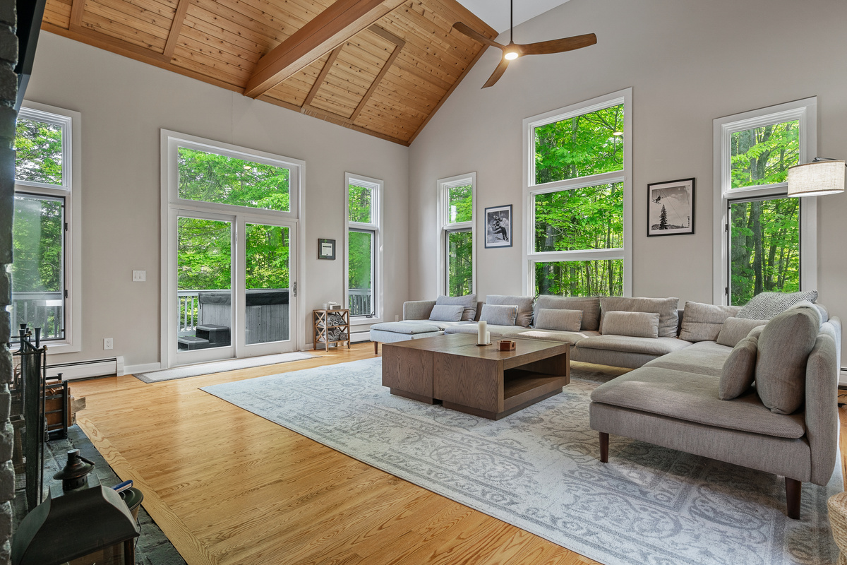 Sun-filled living room with vaulted wood ceiling and windows overlooking the Vermont woods