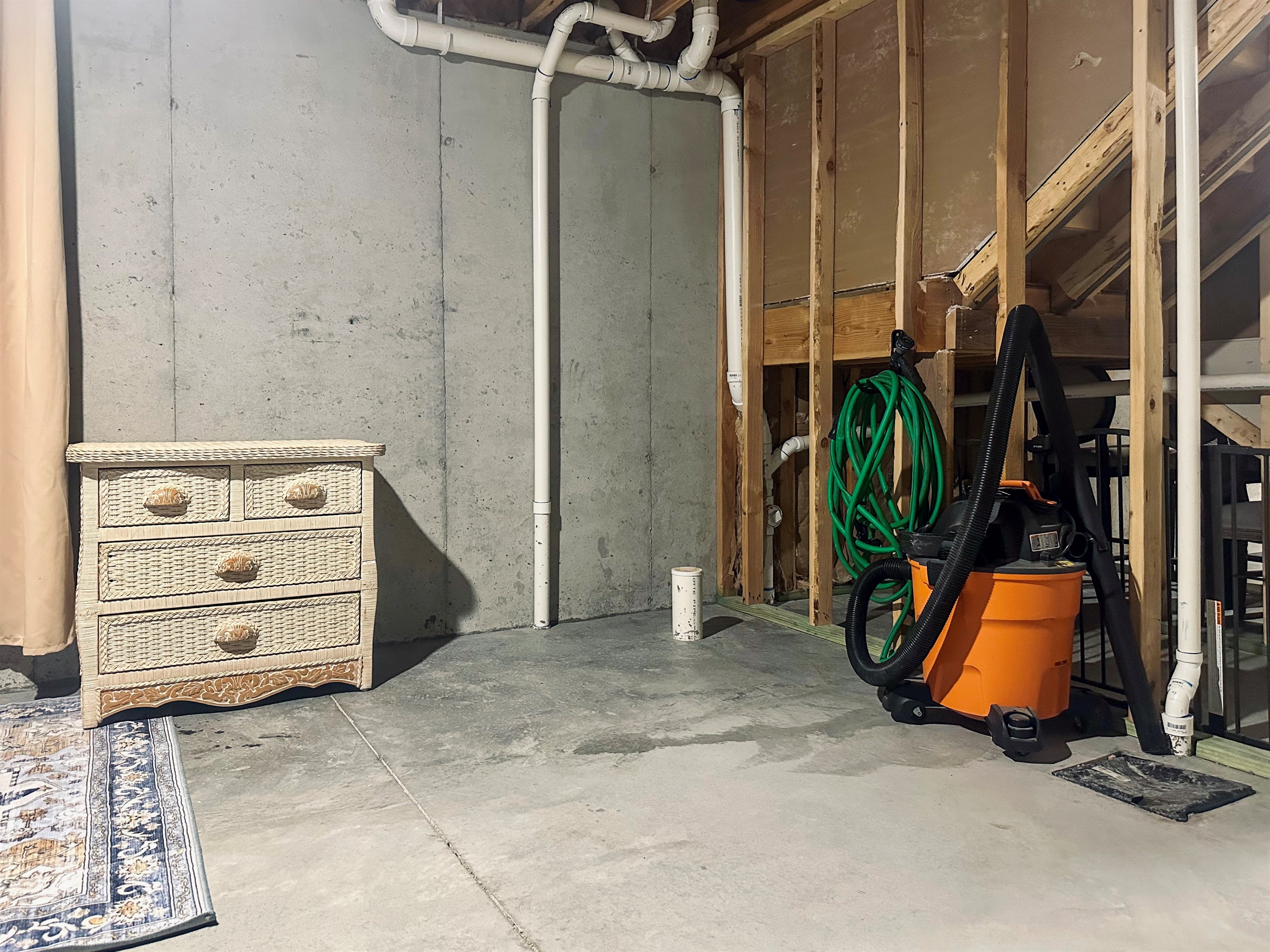 West basement storage area equipped with a shop vac and hose for guest convenience, with generous space for organized belongings.