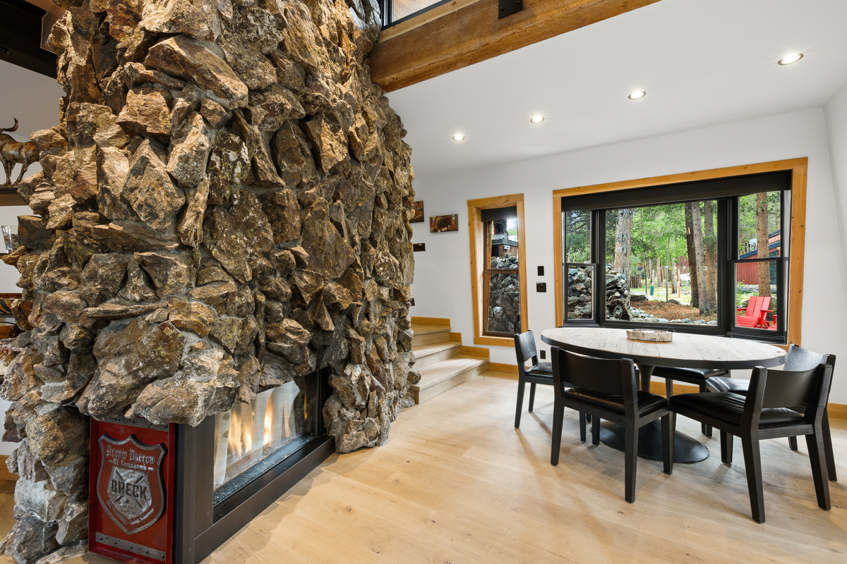A soaring floor-to-ceiling rock fireplace is the center of the home with dining area on right