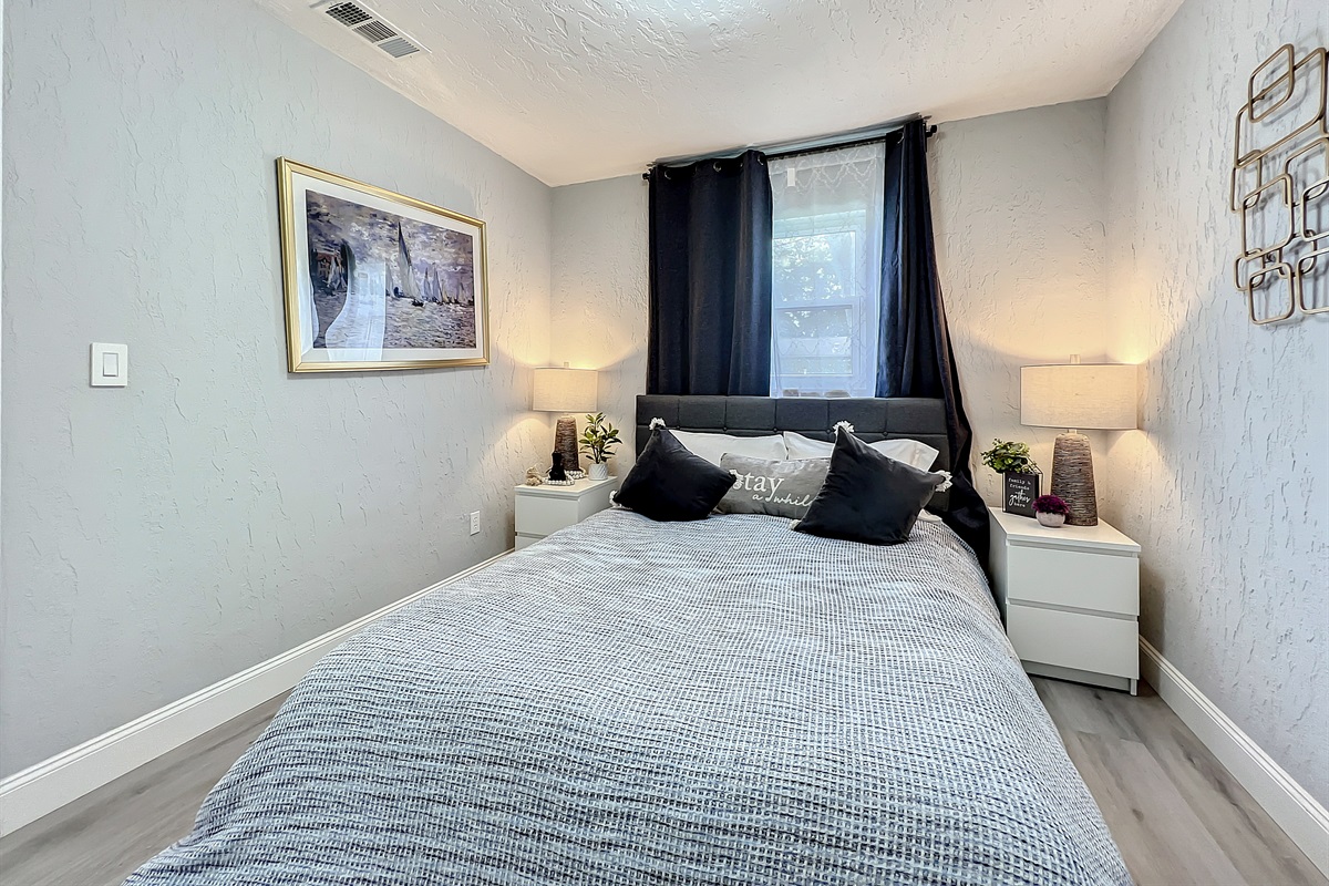Modern bedroom with queen-size bed, grey bedding, and two bedside tables with lamps.