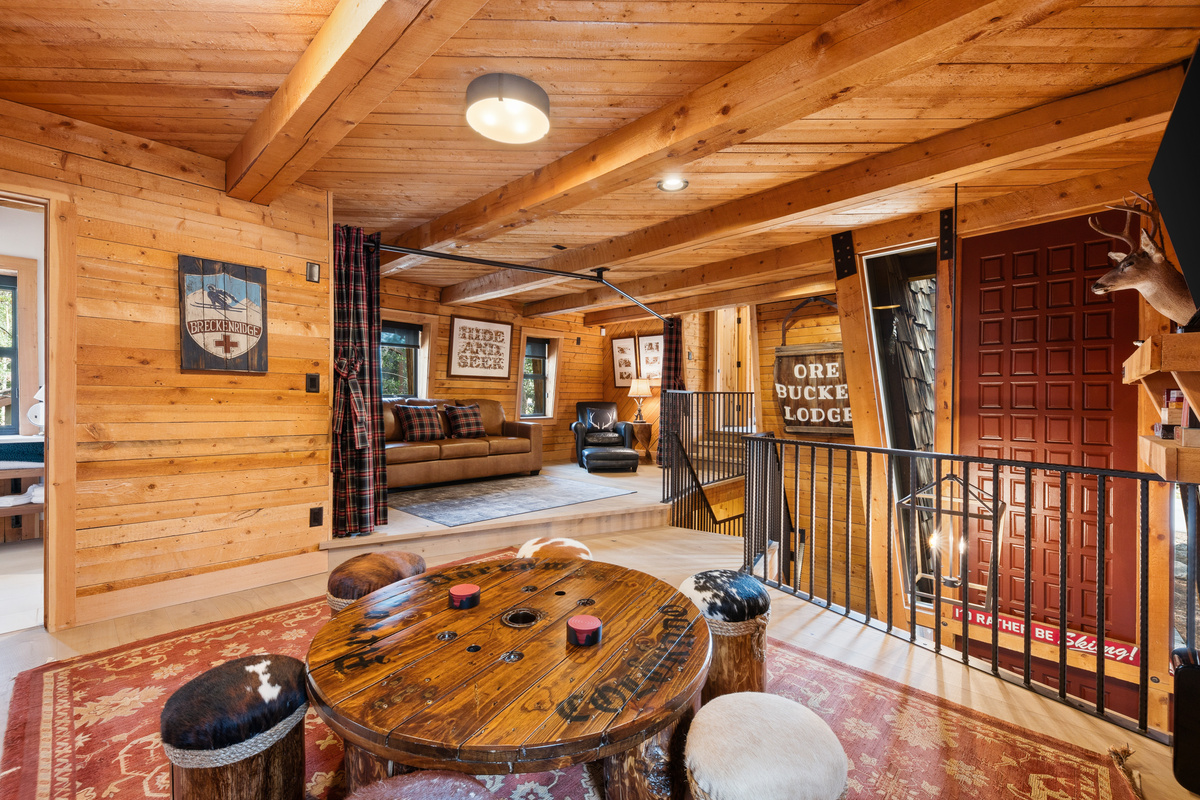 Upper level game room area at top of stairs with tv, game table and desk. Bathroom door partially seen on far left. 